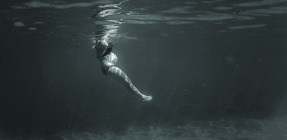 Photo subaquatique en noir et blanc, montrant une femme enceinte dans de l'eau.