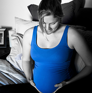 Photo en noir et blanc d'une femme enceinte en débardeur bleu assise sur son lit
